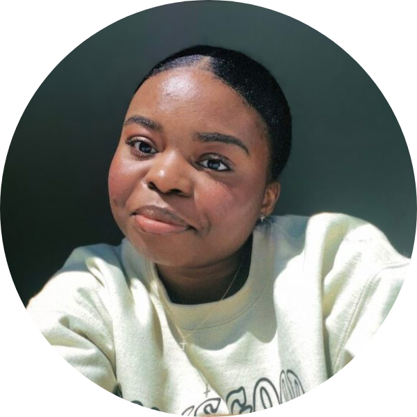 Woman smiling with a cream colored sweatshirt and a shaded background.